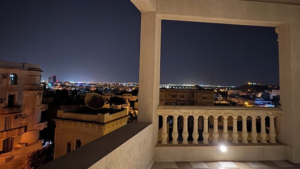 Ein Balkon mit Blick auf eine beleuchtete Stadtlandschaft bei Nacht.