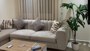Ein modernes Wohnzimmer mit einem Ecksofa, einem Couchtisch, einer Topfpflanze und einem Flachbildfernseher.