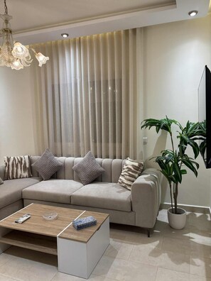 Una sala de estar moderna con un sofá modular, una mesa de centro, una planta en maceta y un televisor de pantalla plana.