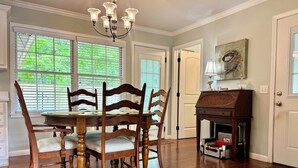 Uma sala de jantar com uma mesa e cadeiras de madeira, um candelabro e um piano.