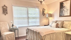 Quarto com uma cama grande, uma cadeira, uma mesinha e um quadro na parede.