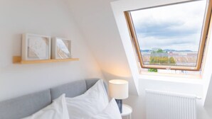 Un dormitorio con tragaluz, una cama, una mesita de noche y un estante fijado a la pared con fotografías enmarcadas.