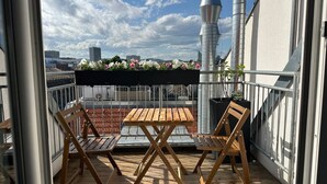 Un balcón con mesa y sillas de madera, barandilla de metal y vistas a la ciudad.