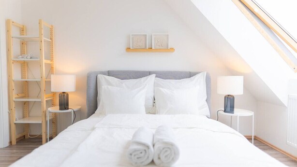Un dormitorio con cama, dos mesitas de noche, un estante con marcos y una estantería de escalera de madera.