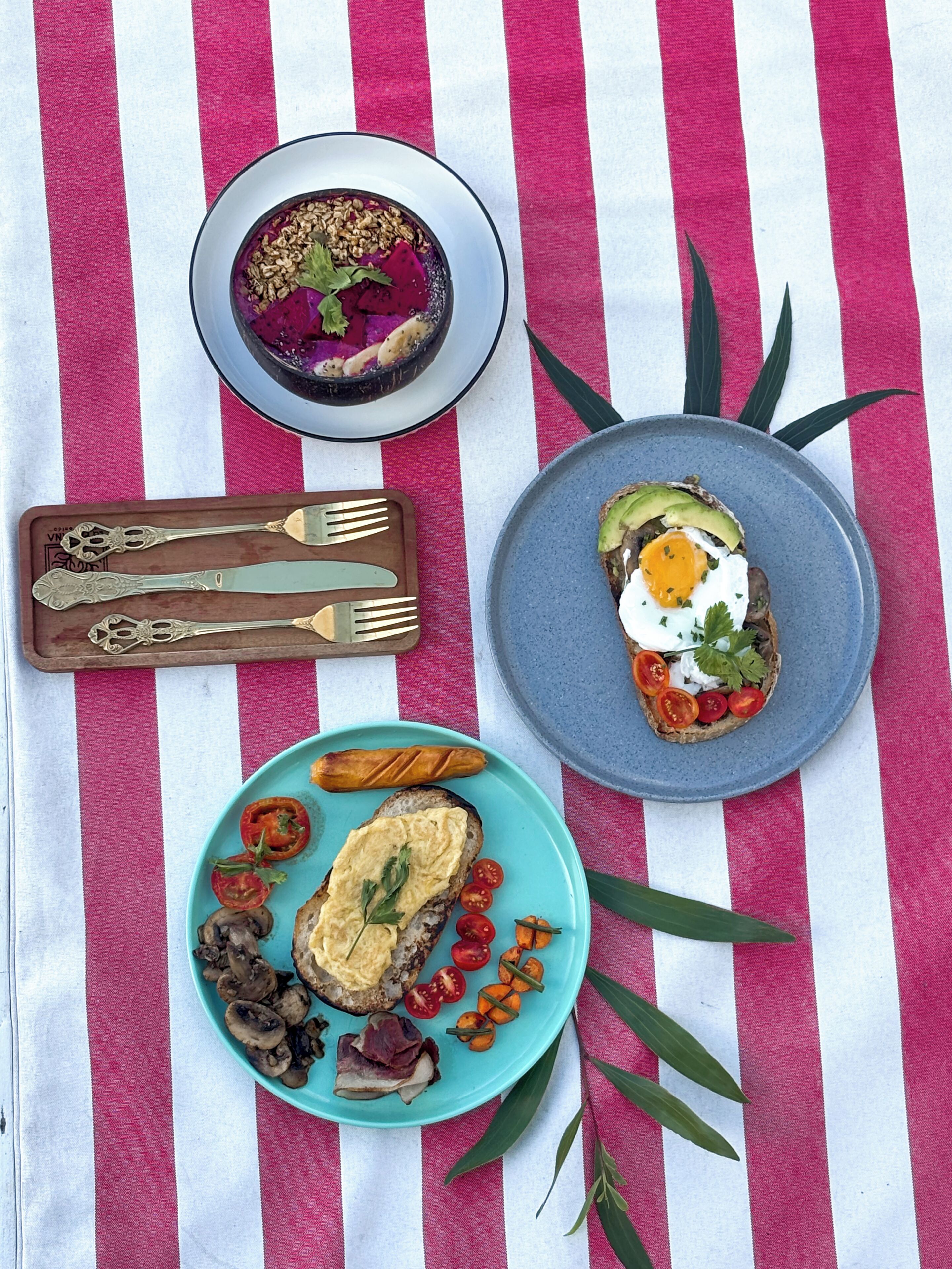 A table with a striped tablecloth, a plate with a fried egg and avocado, a plate with a salad, and a bowl of soup.