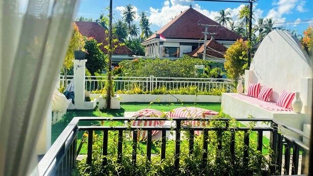 A balcony with a view of a house, a white fence, and a garden with striped umbrellas. - Nusa Penida Homestay (Penida Island)