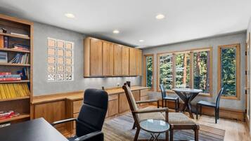A modern interior with a dining area, wooden cabinets, and a view of trees through large windows.