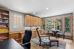 Een modern interieur met een eethoek, houten kasten en uitzicht op bomen door grote ramen.
