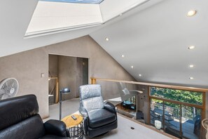 Een moderne loft slaapkamer met dakraam, een balkon met buitenmeubilair en uitzicht op de omgeving.