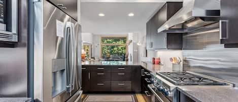 A modern kitchen with stainless steel appliances, a central island, and a view of the outdoors.