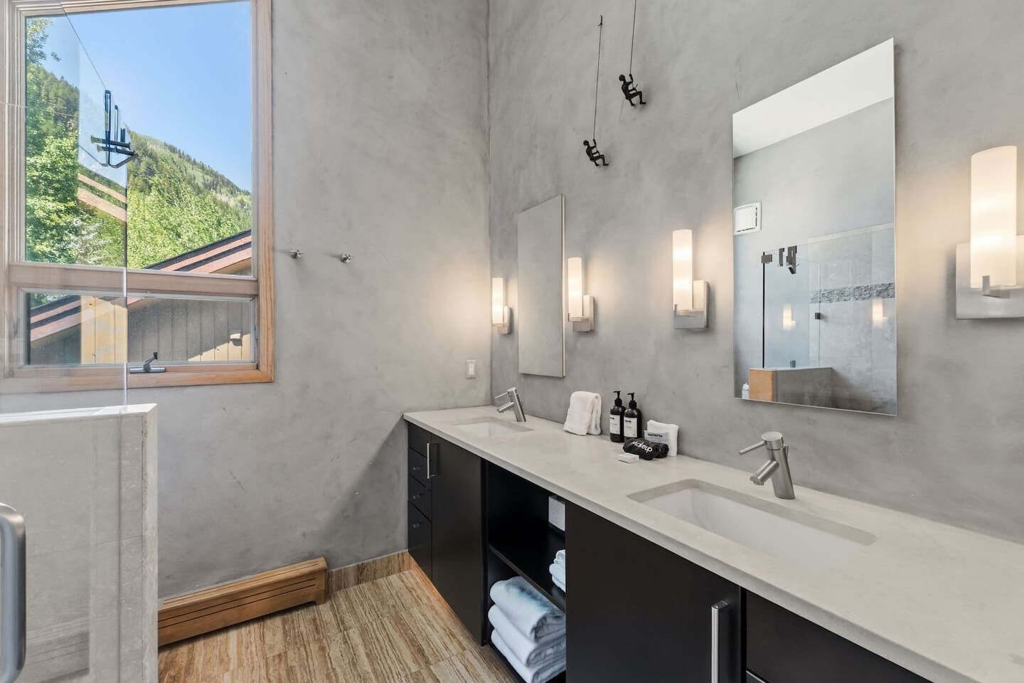 Un baño moderno con dos lavamanos, un espejo grande y vistas a la montaña a través de una ventana.