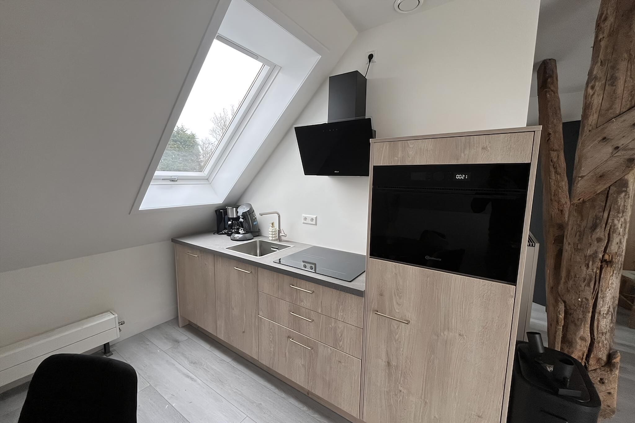 Een compacte keuken met dakraam, inbouwapparatuur en een rustieke houten accent.