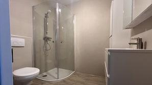 A modern bathroom with a glass-enclosed shower, a toilet, and a white sink.