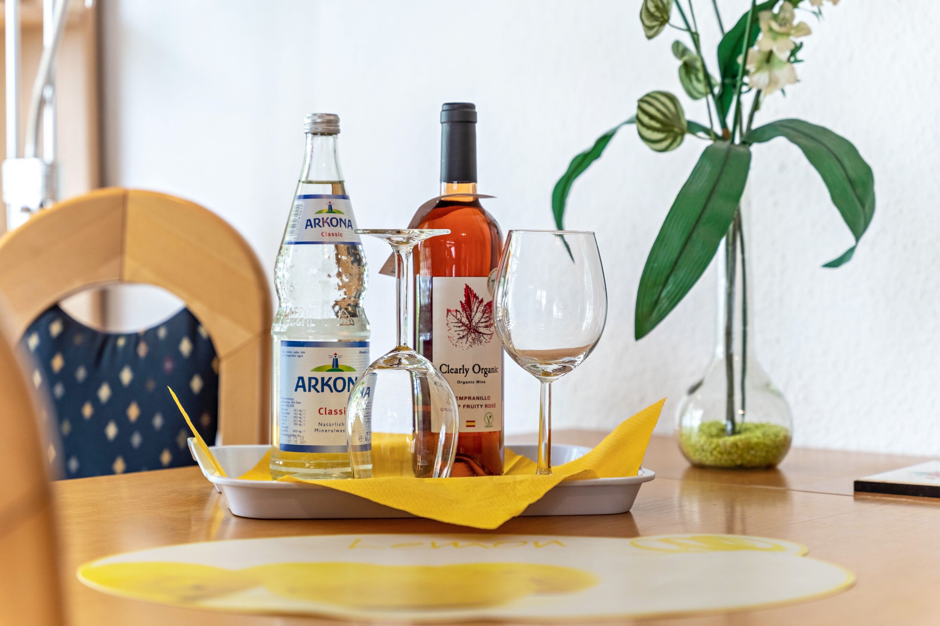 Una mesa con una botella de Arkona Classic, una copa de vino y una copa en una bandeja con servilleta amarilla.