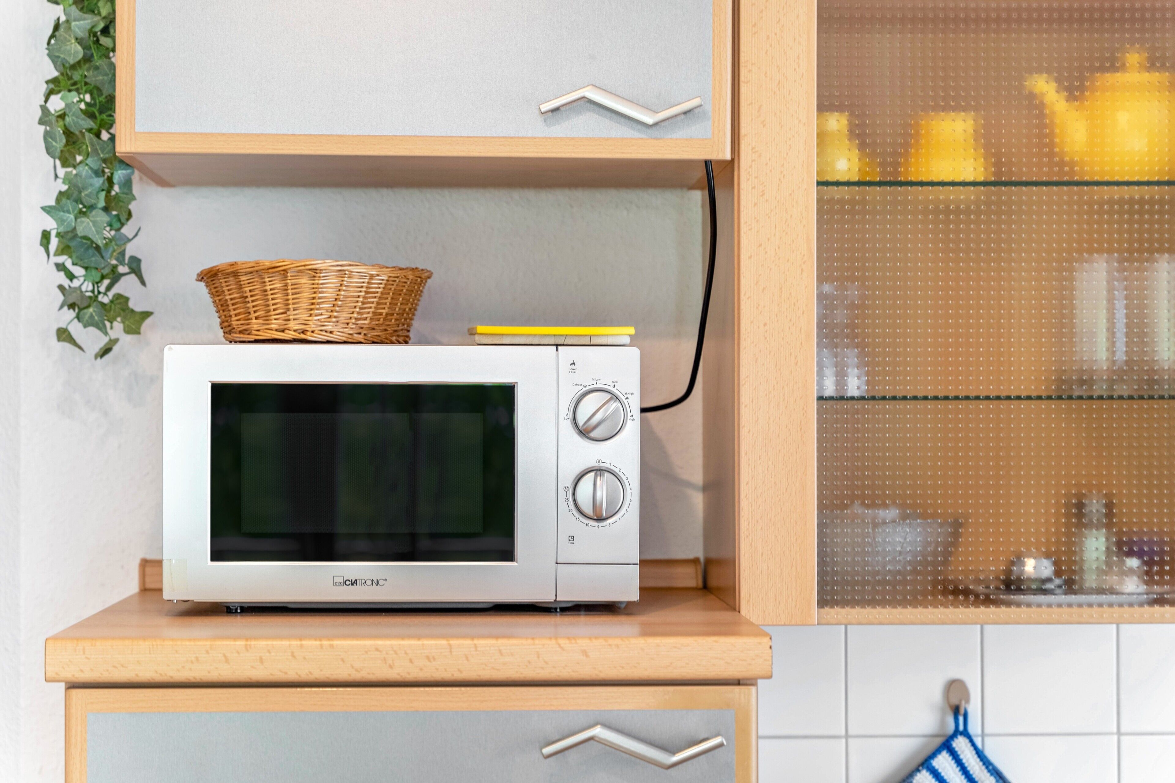 A microwave oven on a wooden countertop with a basket and a yellow object on top.