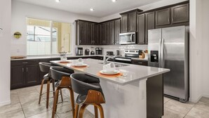 Une cuisine moderne avec des meubles de couleur sombre, des appareils en acier inoxydable et un îlot central doté de tabourets de bar.