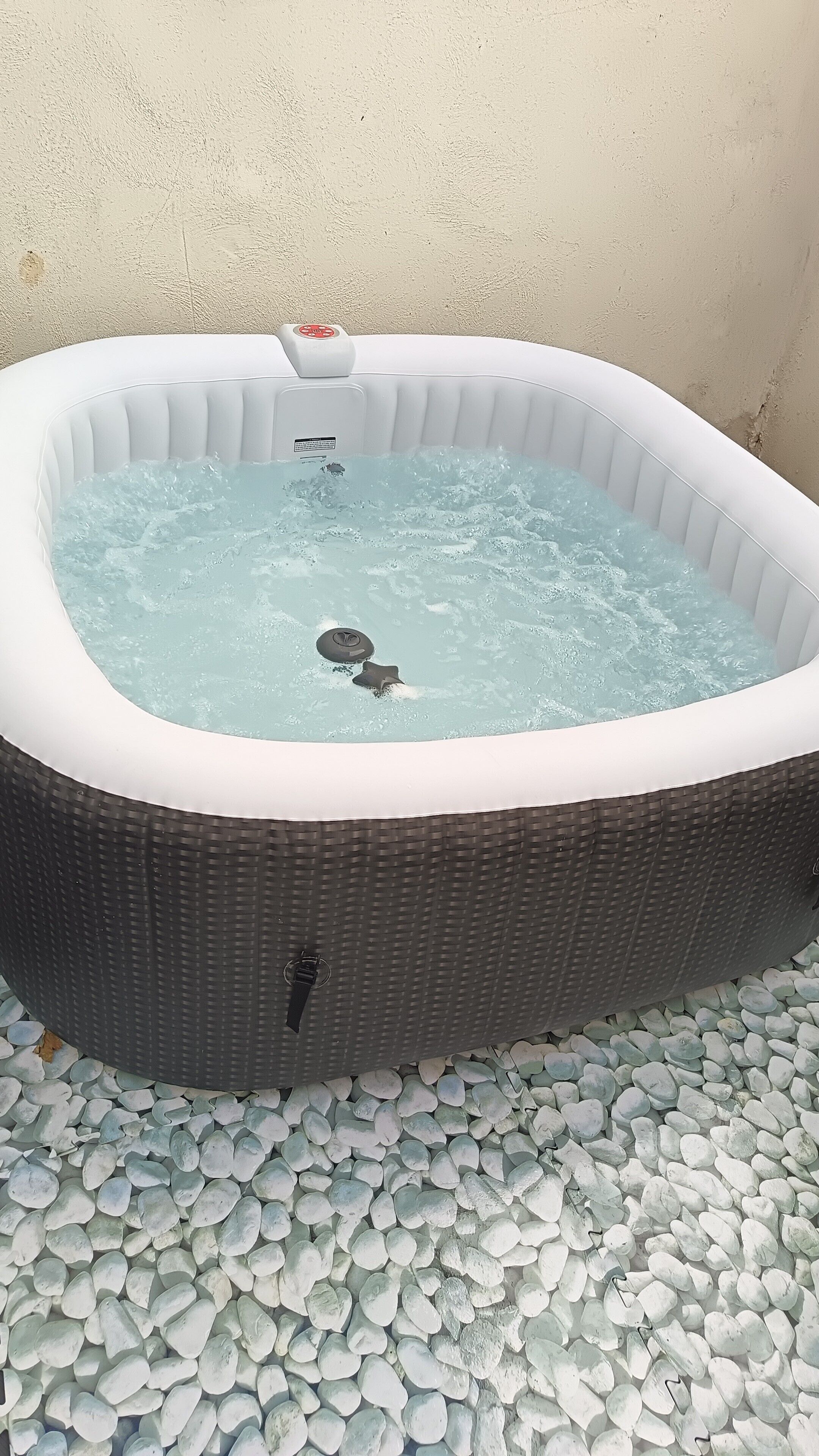 A hot tub with a control panel, surrounded by pebbles.