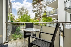 A balcony with a round table and two chairs, overlooking a residential area with trees and buildings. - Apartment Möwe for 4 Guests (40 m²) in Seaside Resort Breege-Juliusruh (Breege)