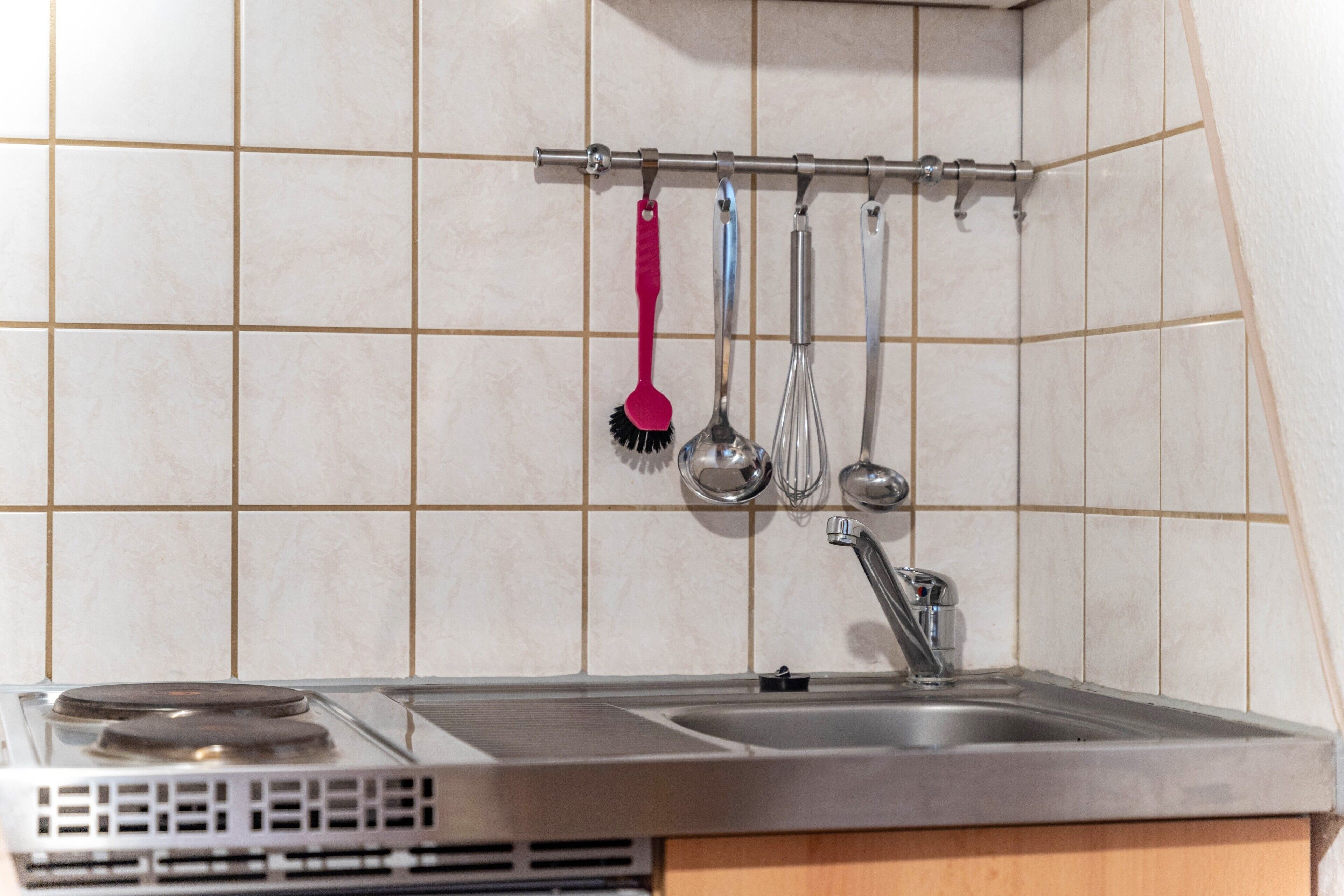 Una cocina con estufa, lavamanos y utensilios colgando.