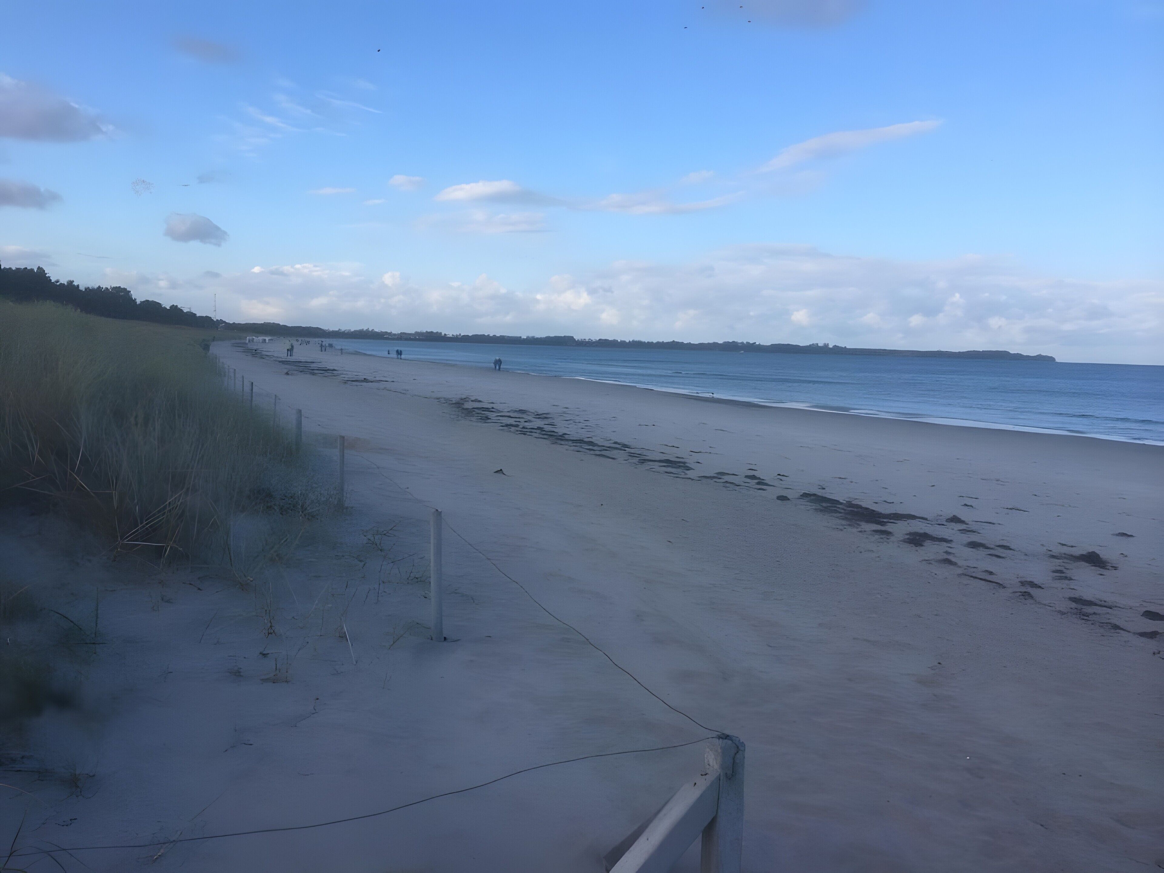 A beach with a fence, sand, and a clear sky.