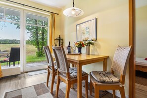A dining area with a wooden table, four chairs, a vase with flowers, and a framed picture on the wall. - Apartment Albatros for 5 Guests (65 m²) with Private Beach Access in Seaside Breege-Juliusruh (Breege)