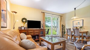 Ein Wohnzimmer mit einer Ledersofa, einem Glastisch, einem Flachbildfernseher und einem Essbereich mit Holztischen und einer Tischplatte.