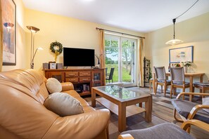 A living room with a leather sofa, a glass coffee table, a flat-screen TV, and a dining area with wooden chairs and a table. - Apartment Albatros for 5 Guests (65 m²) with Private Beach Access in Seaside Breege-Juliusruh (Breege)
