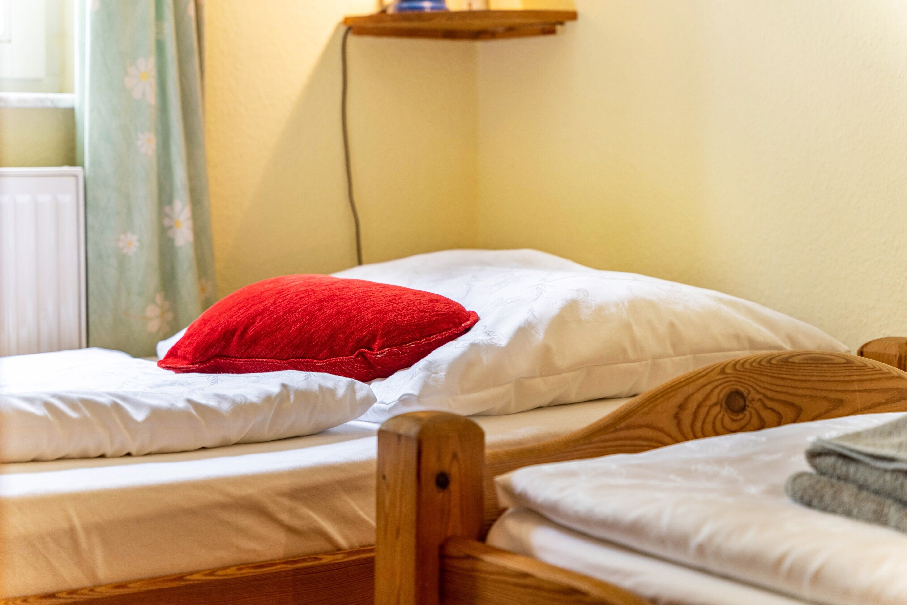 Una cama individual con cabecera de madera, ropa de cama blanca y almohada roja.