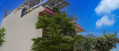 A building with solar panels on the roof, a red roof, and a tree in front.