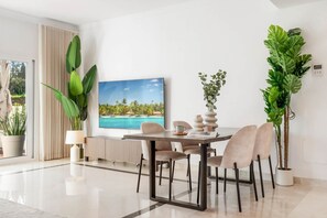 A modern dining area with a table, chairs, a large potted plant, a painting, and a window with curtains. - Luxurious Penthouse - View, Roof Terrace, 3BR/2BA (Benahavís)