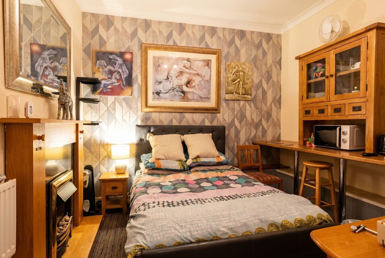Ein Schlafzimmer mit Bett, Nachttisch, Lampe und einem Holzkasten mit Mikrowelle.