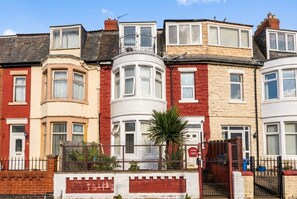 A row of terraced houses with bay windows, a gated entrance, and a palm tree in the foreground. - Characterful Blackpool retreat with courtyard garden for three (Blackpool)