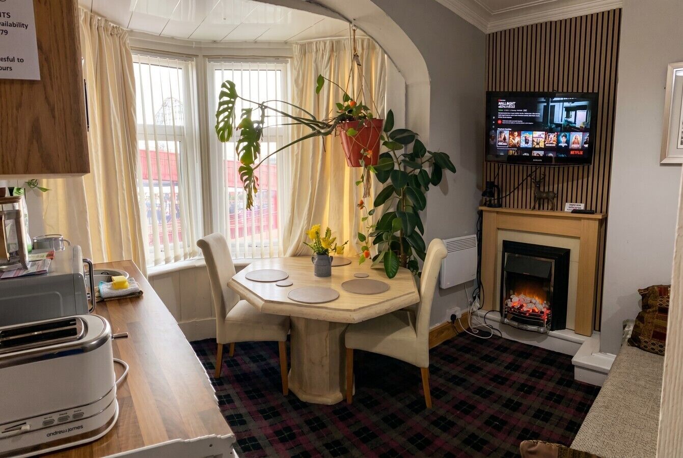 A dining area with a table, chairs, a television, a fireplace, and potted plants.