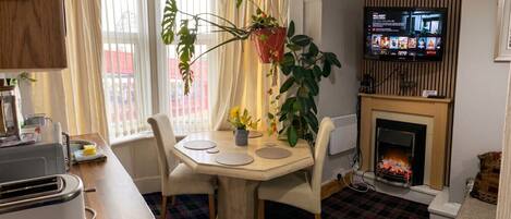 A dining area with a table, chairs, a television, a fireplace, and potted plants.