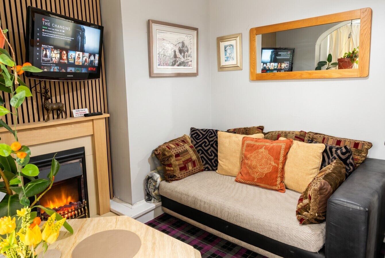 A living room with a sofa, fireplace, television, framed artwork, and a mirror.