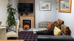 A living room with a fireplace, a flat-screen TV, a sofa with patterned cushions, a chair, and a potted plant. - Fireside South Shore flat · steps from the beach and the Big One (Blackpool)