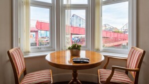 A dining area with a round table and two striped chairs, a potted plant, and a view of a red building through large windows. - Fireside South Shore flat · steps from the beach and the Big One (Blackpool)