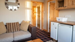 A living room with a sofa, a coffee table, a kitchen area with cabinets and a refrigerator, and a mirror on the wall. - Fireside South Shore flat · steps from the beach and the Big One (Blackpool)