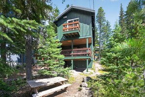 A multi-level cabin with a wooden deck and a picnic table in a forested area.