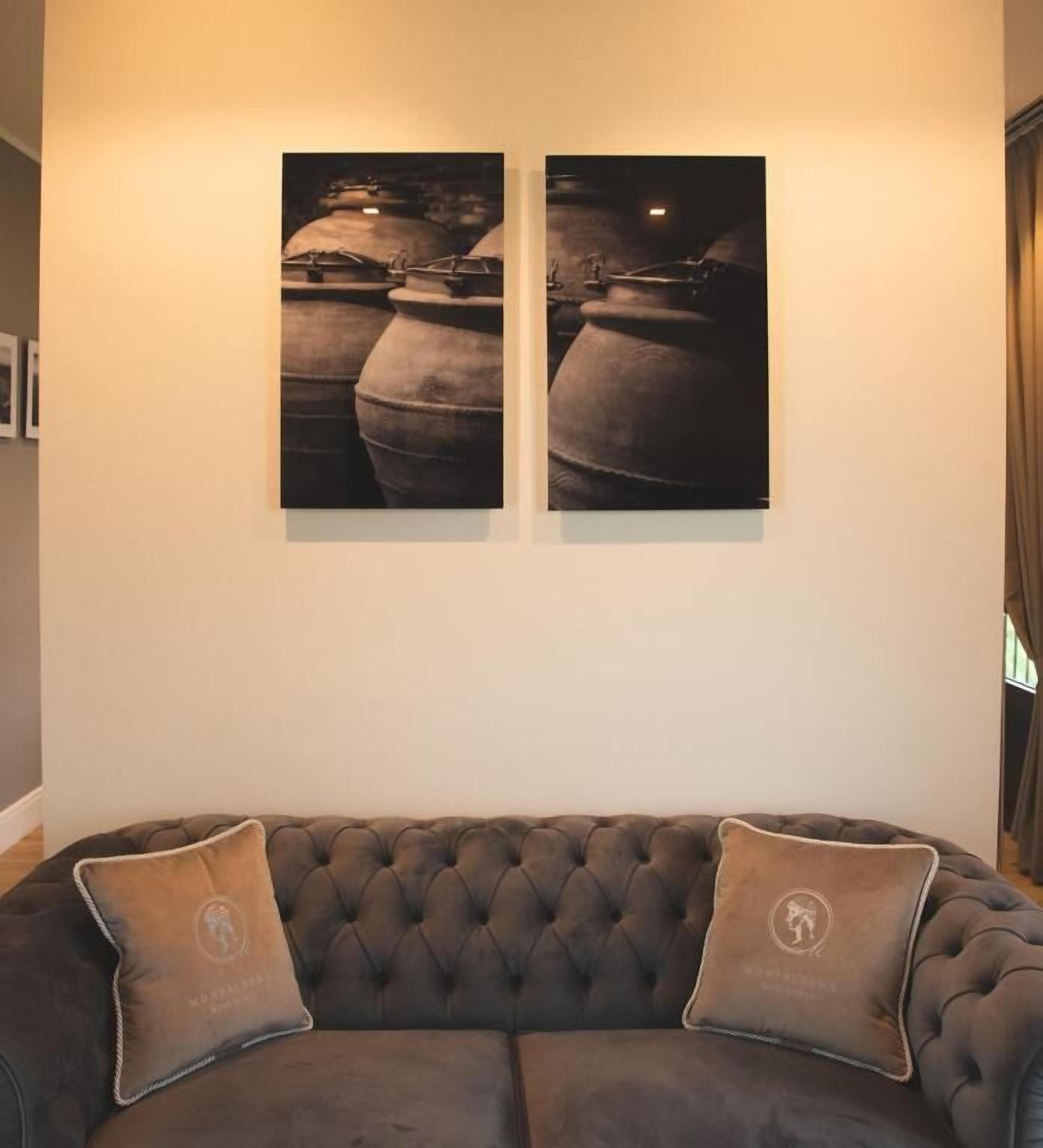 A room with a dark brown sofa, two cushions, and two framed photographs on the wall.