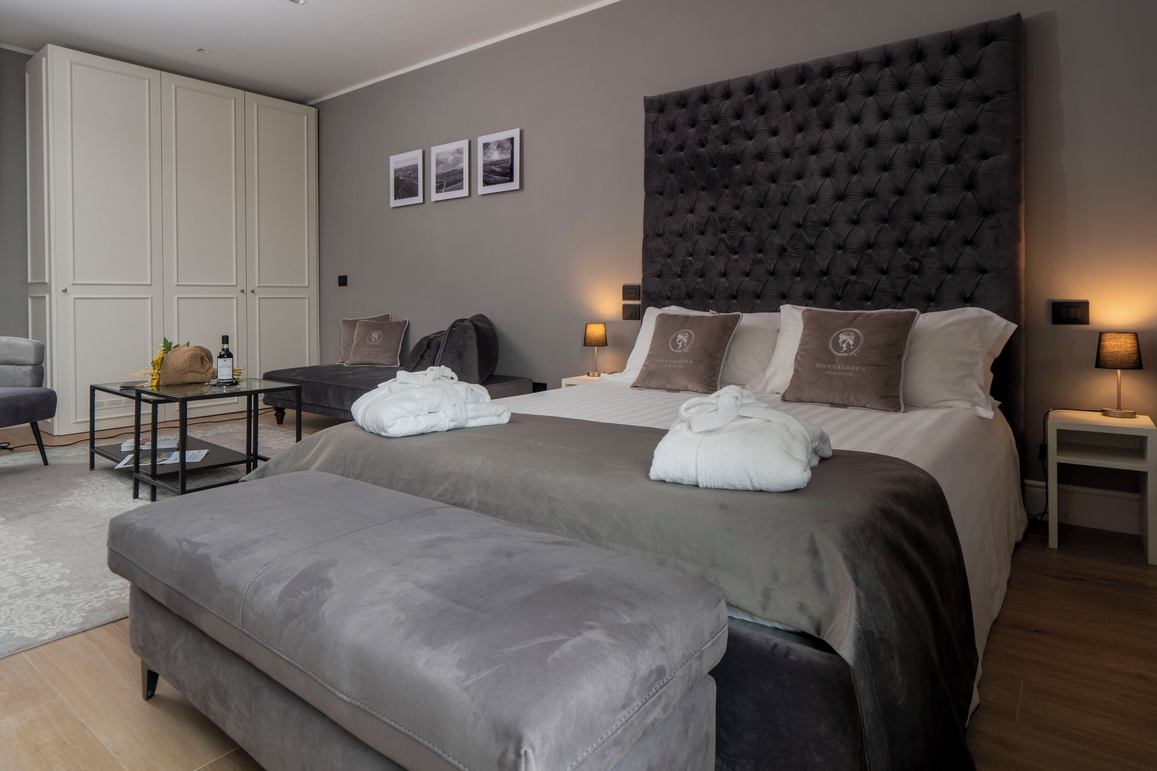 Ein modernes Hotelzimmer mit einem großen Bett, einem grauen Sofa, einem kleinen Tisch mit einer Flasche und einem Kleiderschrank.