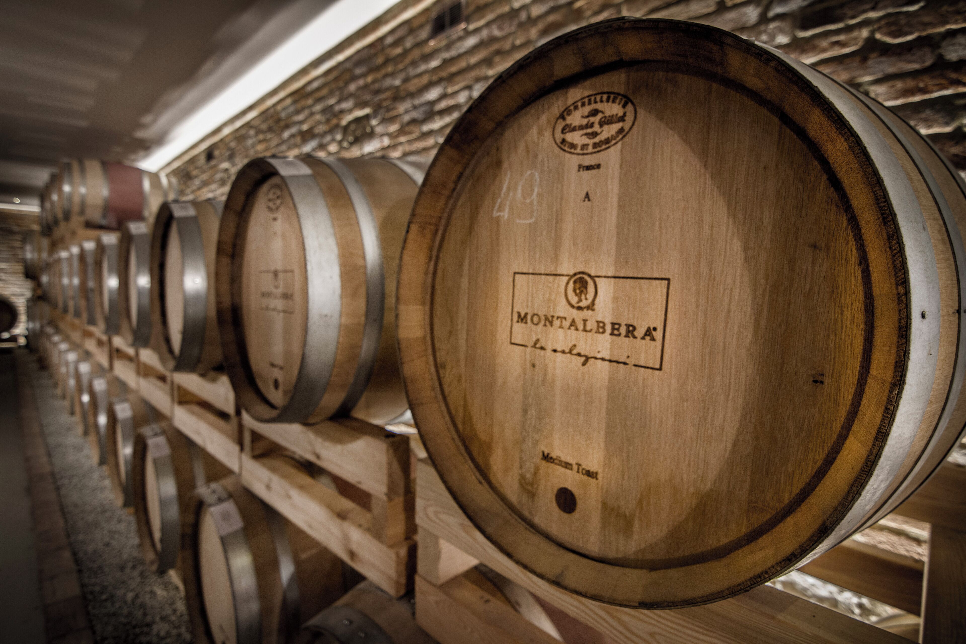 Wooden wine barrels lined up in a row, each with a label.