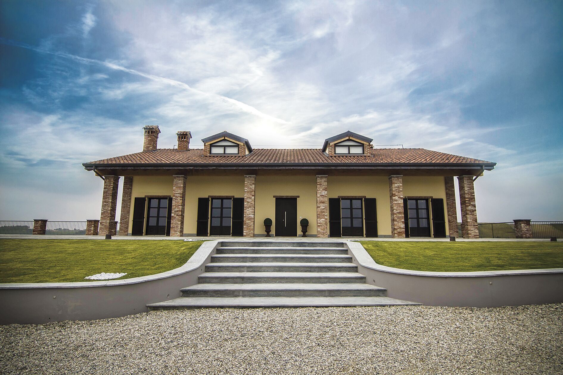 Une maison à deux étages, dotée d’une façade symétrique, d’une entrée centrale et d’un escalier menant à la porte d’entrée.