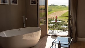 A modern bathroom with a freestanding bathtub, a glass table with a bottle, and a balcony with a table and chairs. - Montalbera Wine Suites (Castagnole Monferrato)