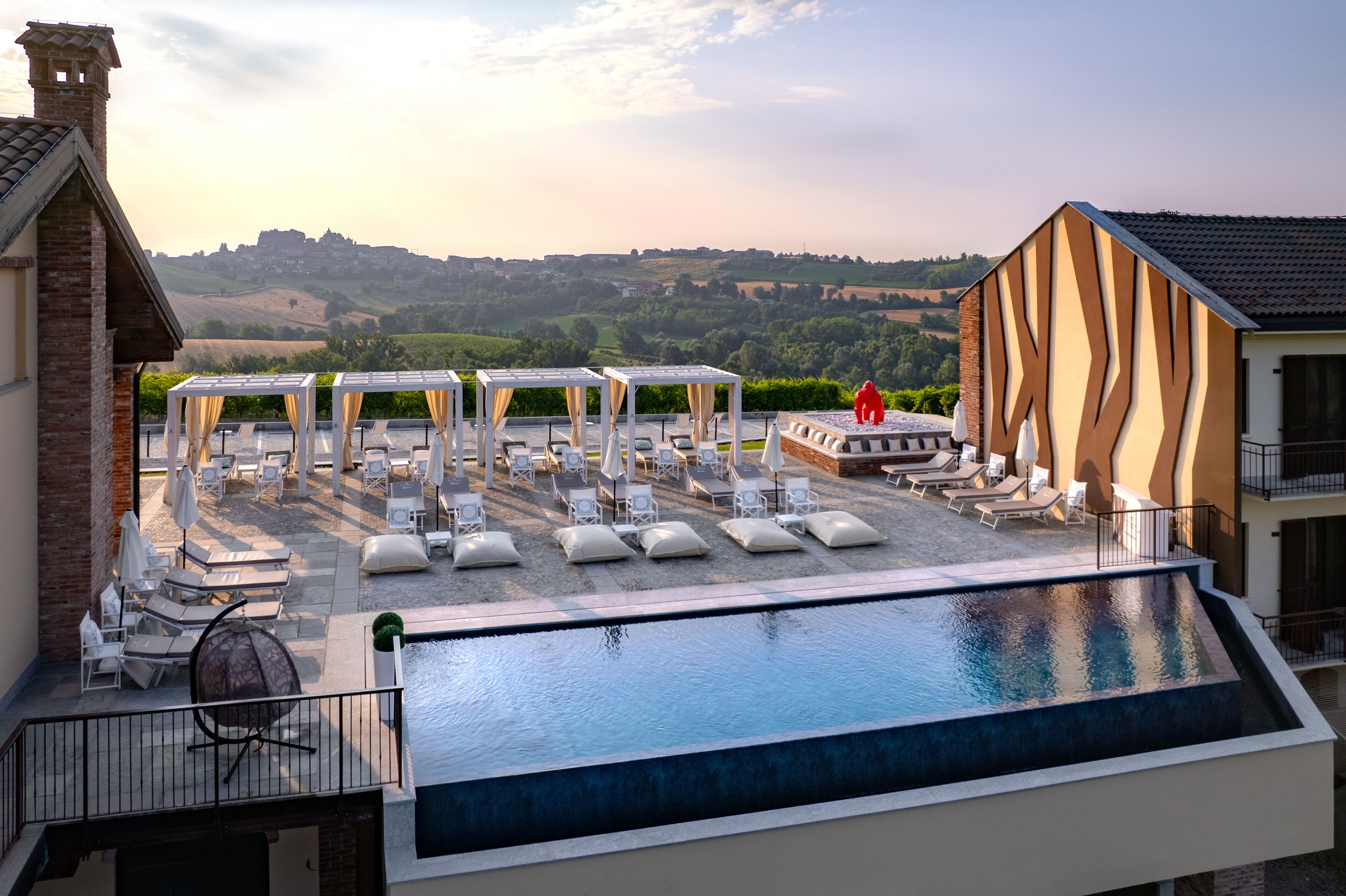 A rooftop pool with lounge chairs and umbrellas, a view of the countryside, and a building with a unique facade.