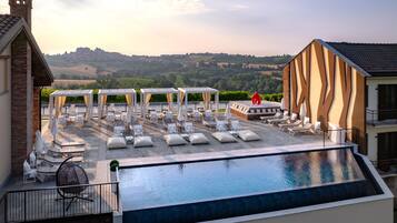 A rooftop pool with lounge chairs and umbrellas, a view of the countryside, and a building with a unique facade.