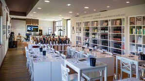 A wine tasting room with white tables, chairs, and a wine rack filled with bottles. - Montalbera Wine Suites (Castagnole Monferrato)