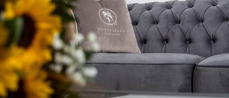 Ein graues, gestepptes Sofa mit einem Kissen, das das Logo von 'Montalbera Wine Suites' zeigt.