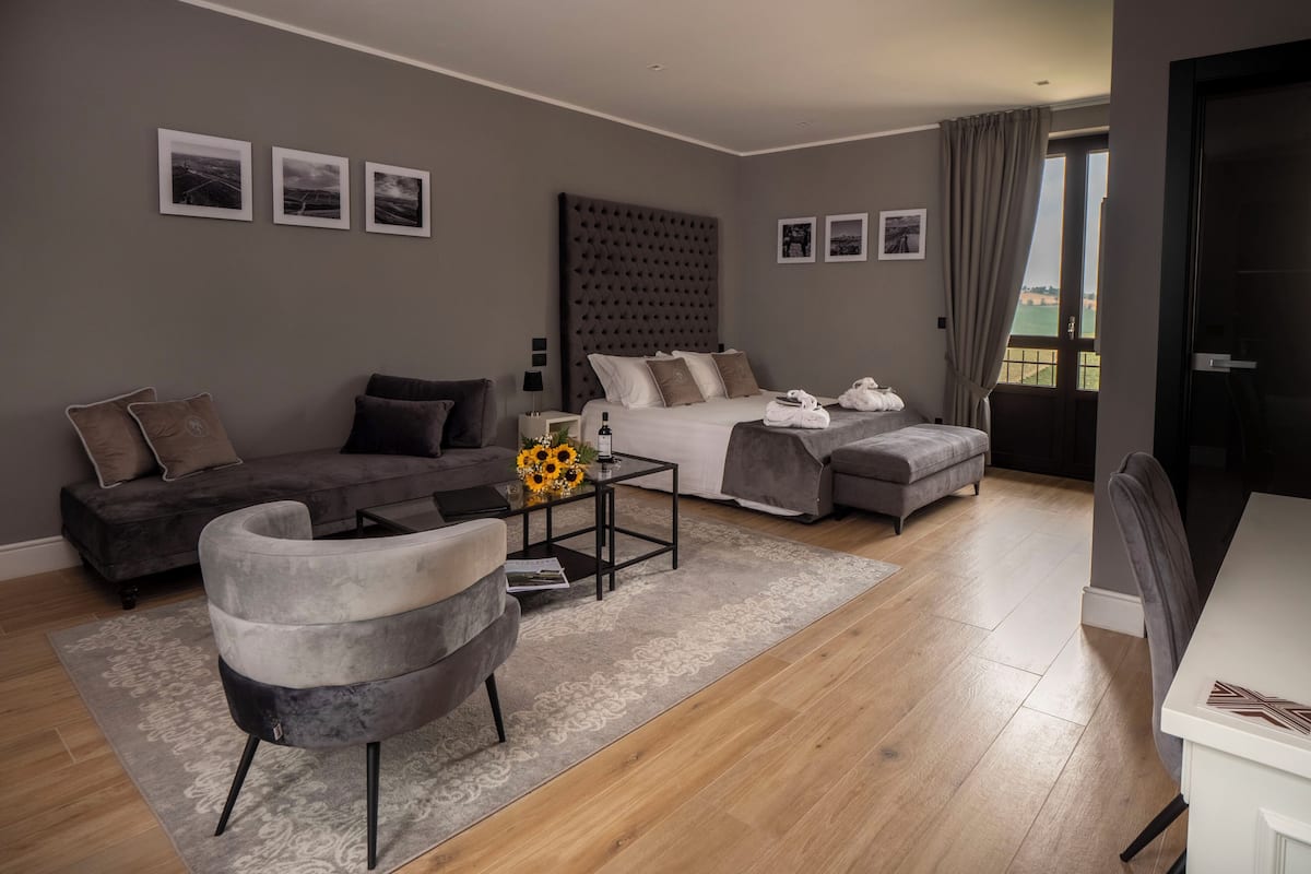 Ein modernes Hotelzimmer mit einem großen Bett, einer Couch, einem Sessel und einem kleinen Tisch mit einer Vase voller Sonnenblumen.