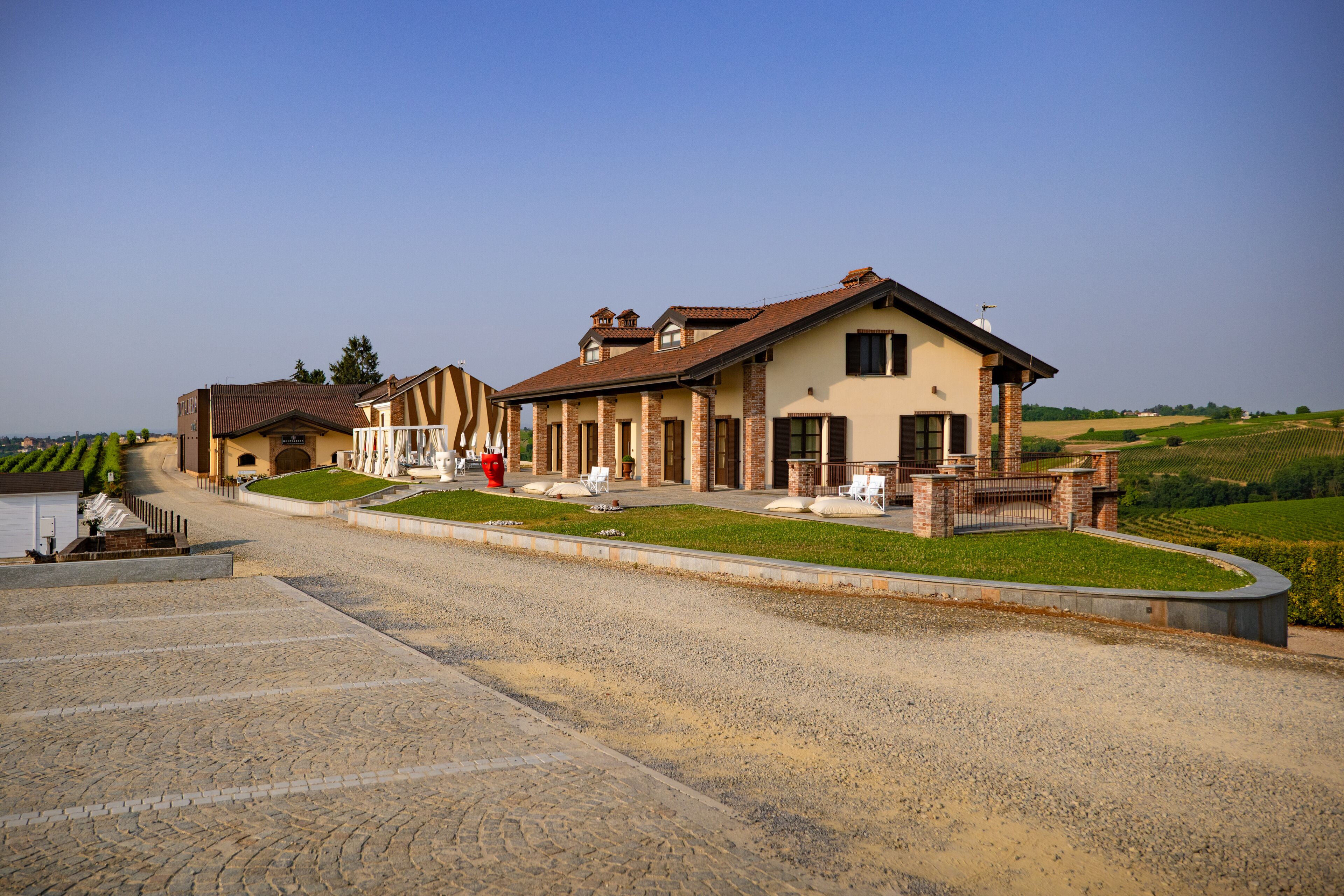 A large building with a driveway, a lawn, and a vineyard in the background.